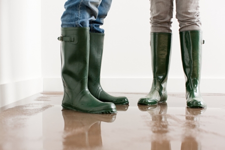 Two people in rubber boots standing on a flooded home floor. | American Pest Control
