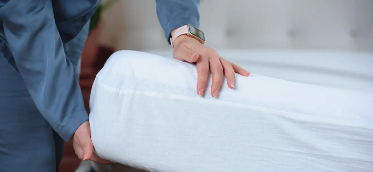 A hospitality worker puts a mattress cover on a bed. Mattress encasement can protect against bed bug infestations.
