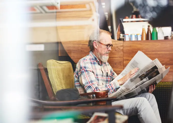 Man reading the newspaper in a cafe couch. Bed Bugs can hitch a ride in clothing, particularly when visiting public places.