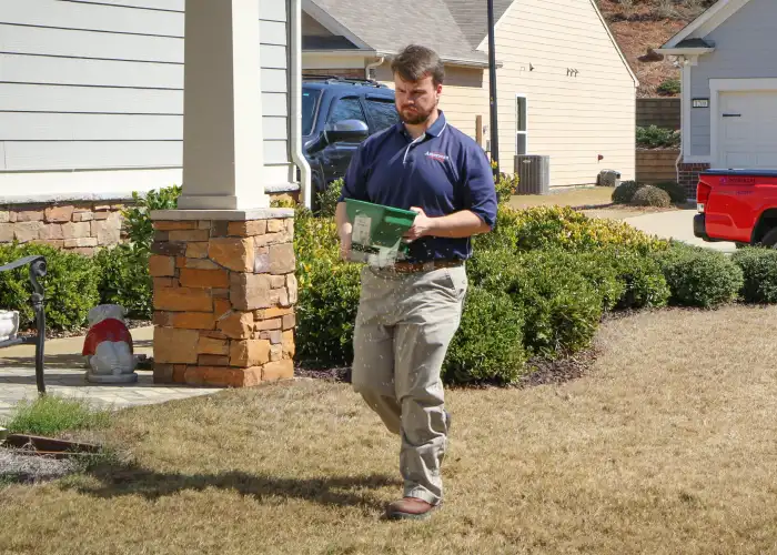 An American Pest Control, Inc. technician distributing granular pest control treatments in a yard to protect against crickets