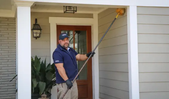An American Pest Control, Inc. service technician cleaning cobwebs from a home in Social Circle, GA