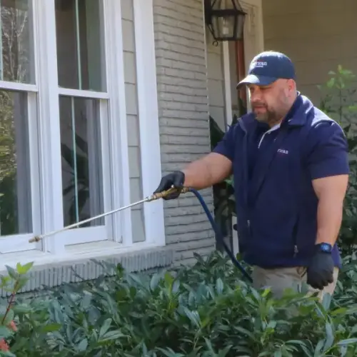 An American Pest Control, Inc. technician applies pest treatment to the exterior of a residential home.