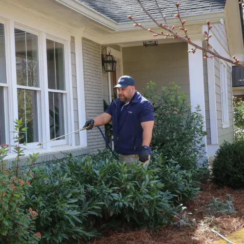 An American Pest Control, Inc. technician applies pest treatment to the exterior of a residential home.